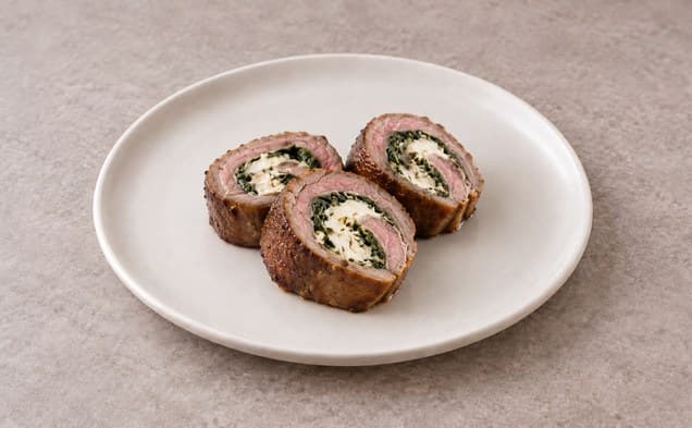 A serving of lamb and fresh goat cheese roulade on a plain white dish